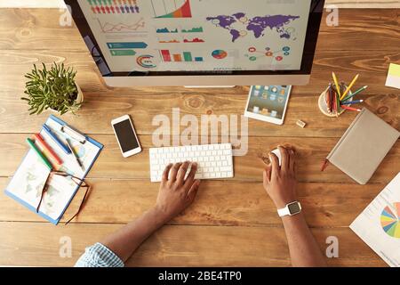 Top view of afro american businessman working on the computer while working remotely at home. Home office workplace. Desk with computer, smartphone, digital tablet. Cropped photo. Freelance Stock Photo