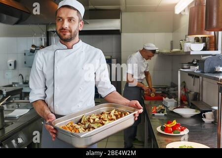 Smiling caucasian cook wearing uniform is doing his job. He prepares the necessary ingredients for his signature dish. Front view. Cooking concept Stock Photo