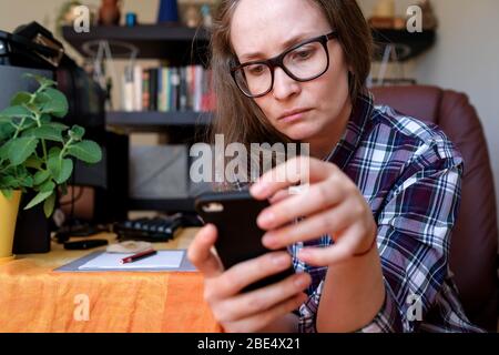 A woman works at home, reads from the phone. Freelancer. In the background a cozy room. Stock Photo