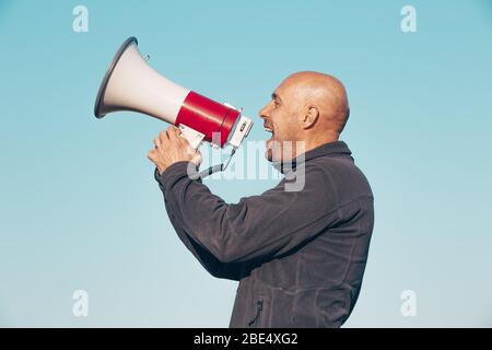 Cheerful man shouting, screaming through a megaphone, announcing something news, announcments concept Stock Photo