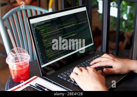 Developer programmer with laptop. Program code and script data on screen. Young freelancer in glasses working on project in cafe. Back view over the Stock Photo