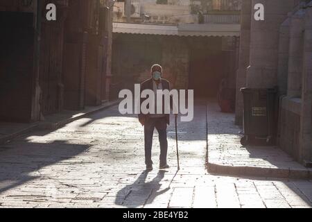 Jerusalem, Israel. 12th Apr, 2020. An elderly man wears a face mask as he walks across an empty street. The Israeli government approved a tight quarantine of several areas of Jerusalem including the historic Old City, in a bid to slow the spread of the coronavirus. Credit: Ilia Yefimovich/dpa/Alamy Live News Stock Photo