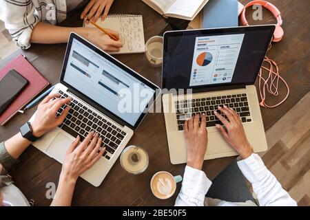 Tope view close up of women typing on laptop computers over cafe table with coffee cups Stock Photo
