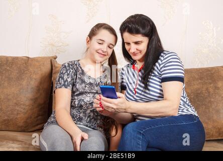 mom and daughter look at the smartphone display sitting on a sofa at home. coronavirus quarantine. Stock Photo
