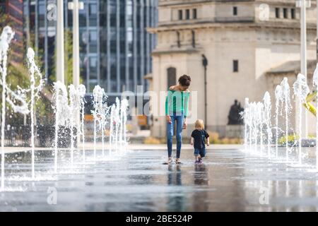 Birmingham, UK. 12th Apr, 2020. Twelve-year-old Mia takes her 18-month-old brother Jasper for their daily exercise walk through the fountains in Centenary Square, Birmingham city centre. Their family lives nearby. Easter Sunday has begun as a warm and sunny day. [Parental permission granted] Credit: Peter Lopeman/Alamy Live News Stock Photo