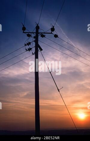 Wooden electricity distribution pole and cables in silhouette against an evening sunset sky, England, UK Stock Photo