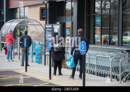 Cumbernauld, UK. 12th Apr, 2019. Pictured: Customers queue outside a shop whilst keeping social distancing. Scenes during the Coronavirus (COVID-19) lockdown from a retail park in Cumbernauld. Shoppers queue outside to get their bargains and supplies for the Easter Sunday festive period. Credit: Colin Fisher/Alamy Live News Stock Photo