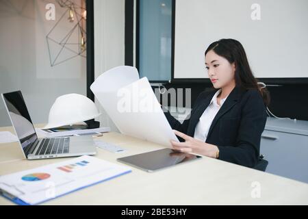 Asian women engineering holding blueprints and have hard hat on table  for working at office Stock Photo