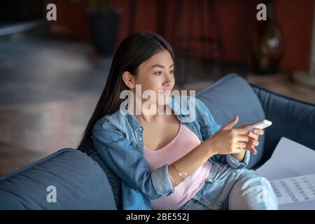 Young woman sitting on sofa, holding remote control Stock Photo