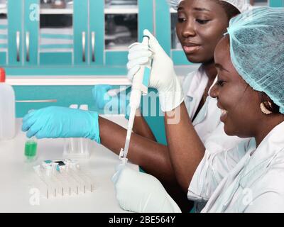 Two African scientists, technical assistants or graduates in lab coats and gloves perform PCR testing of patient samples in test lab or medical facili Stock Photo