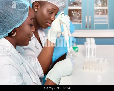 Two African scientists, technical assistants or graduates in lab coats and gloves perform PCR testing of patient samples in test laboratory or medical Stock Photo