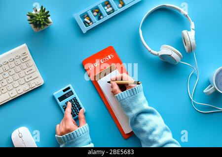 Creative flat lay with pen and calculator in hands to calculate drug costs. Keyboard, calculator, pills and pill case on mint blue background. Checkin Stock Photo