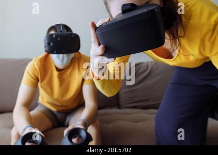 What to do at home on self-isolation. In the foreground, a girl with glasses. In the background, a guy with masks. Stock Photo