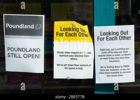 Notices on Poundland shop during the 2020 coronavirus Covid-19 pandemic, saying it is open, maintain social distancing, three items only Stock Photo
