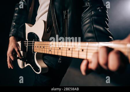 Close-up view of rock musician mans hands masterfully playing electric guitar. Fingers tapping strings in smoky spotlight during concert on stage. Stock Photo