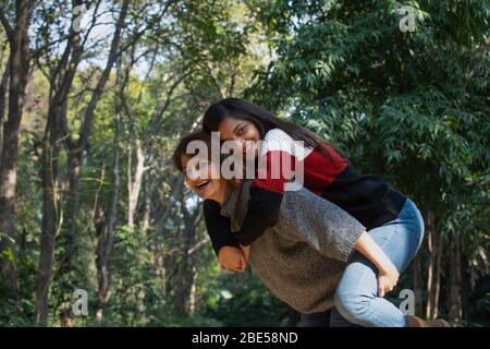 Young woman giving her younger sister a piggy back ride in the park. Stock Photo