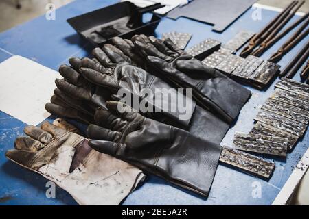 Fire Protection gloves, pliers and many pieces of steel on the desk to be used in electric metal welding workshop Stock Photo