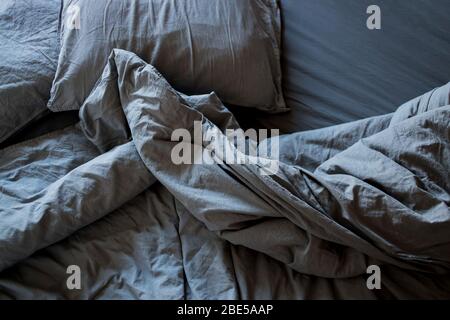 Top view crumpled bed in the morning after sleep. Gray cotton sheet and blankets on the bed Stock Photo