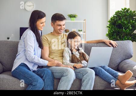 Happy family chatting online using laptop while sitting with baby on sofa at home. Stock Photo