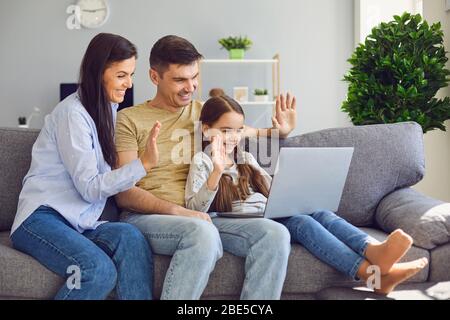 A happy family waving online communication using a laptop while sitting with the child on the couch at home Stock Photo