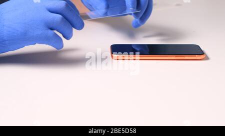 male hands in blue gloves replaces a broken tempered glass screen protector for a smartphone. A man prepares a smartphone to replace glass. Smartphone Stock Photo