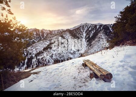 Wooden bench and panoramic view of high mountain range of Zaili Alatay and at sunrise from Kok Zhaylau trail in Almaty, Kazakhstan Stock Photo