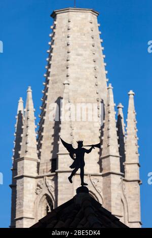 Weather vane trumpeting angel silhouette on roof top with Church of Sant Feliu (Saint Felix) tower in the background in Girona, Catalonia, Spain Stock Photo