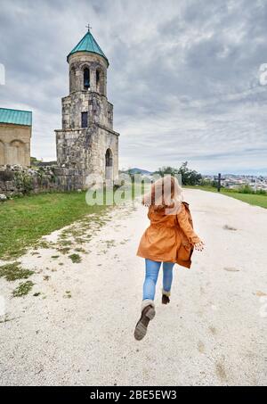 Woman running to the Chapel tower of Bagrati church at overcast sky in Kutaisi, Georgia Stock Photo