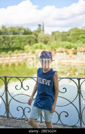 Young handsome teenage boy wearing a summer hat standing in front of a lake suspiciously looking into the camera Stock Photo