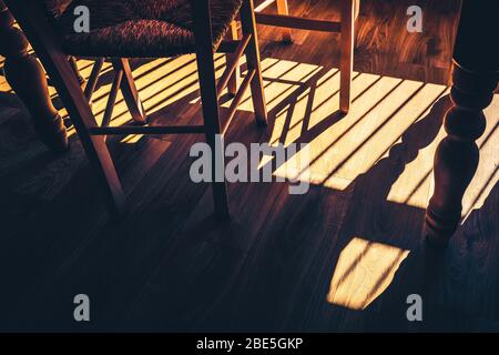 Shadows on a wooden kitchen floor from window blinds and the legs of the table and chairs. Stock Photo