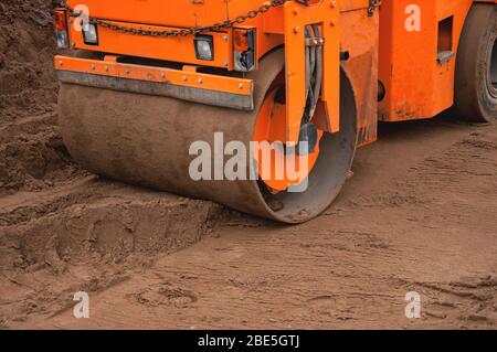 A small road roller rolls soil for a new road. Construction machinery at work. Road construction equipment Stock Photo