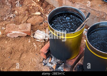Bitumaning the mastics in yellow jars. Material for waterproofing the foundation. The mastika in the jars is heated on fire. Stock Photo