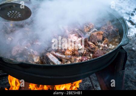 The meat is cooked in a cauldron on fire. Cooking a national dish. Stock Photo