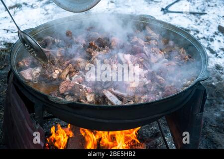 The meat is cooked in a cauldron on fire. Cooking a national dish. Stock Photo