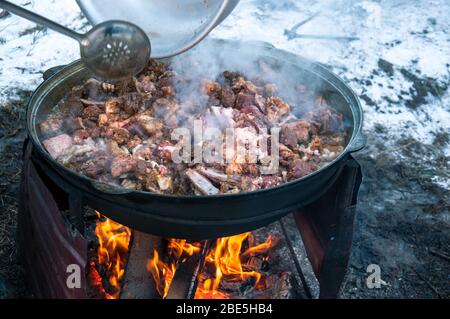 The meat is cooked in a cauldron on fire. Cooking a national dish. Stock Photo