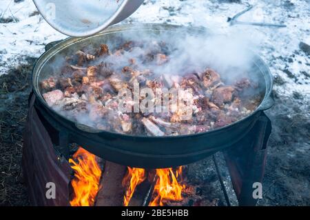 The meat is cooked in a cauldron on fire. Cooking a national dish. Stock Photo