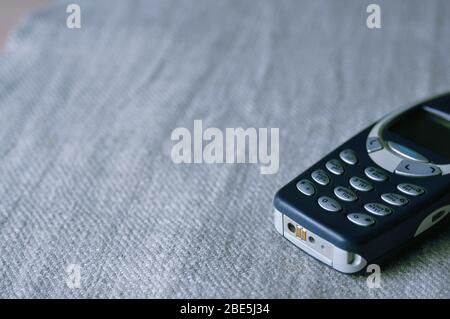 Old push-button mobile phone close-up on a fabric background. Old cell phone model. Technologies of the last century. Stock Photo