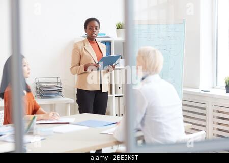 Portrait of successful African-American businesswoman giving presentation to colleagues while standing by whiteboard during meeting in conference room Stock Photo