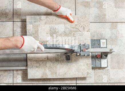 A man is cutting a ceramic tile with a tile cutter. Stock Photo
