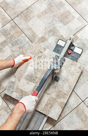A man is cutting a ceramic tile with a tile cutter. Stock Photo