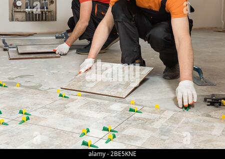 Two workers are installing ceramic tiles on the floor. Stock Photo