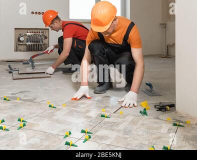 Two workers are installing ceramic tiles on the floor. Stock Photo