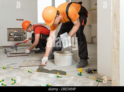 Two workers are installing ceramic tiles on the floor. Stock Photo