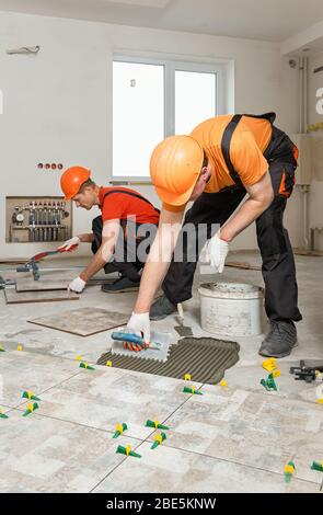 Two workers are installing ceramic tiles on the floor. Stock Photo