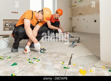 Two workers are installing ceramic tiles on the floor. Stock Photo