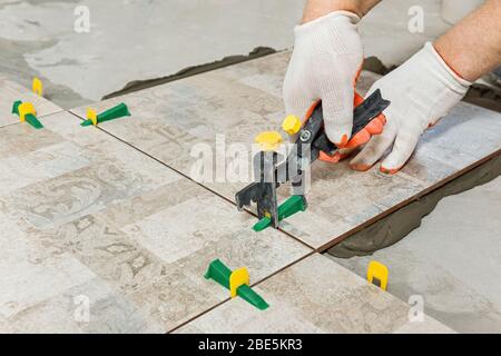 A worker is leveling the ceramic tile with wedges and clips. Stock Photo