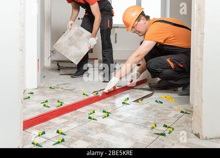 Two workers are installing ceramic tiles on the floor. Stock Photo