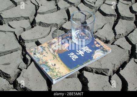 close up of book and cup in the dry land, creative images, metaphor of knowledge as spring water, as is indispensable to the people. Stock Photo