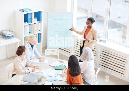 Portrait African-American female manager presenting project plan to group of colleagues and smiling happily while standing by whiteboard during meetin Stock Photo