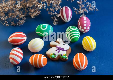 The attributes of the chrestian Easter holiday are colored eggs and gingerbread in the form of a rabbit on a dark blue table. Contrast Stock Photo